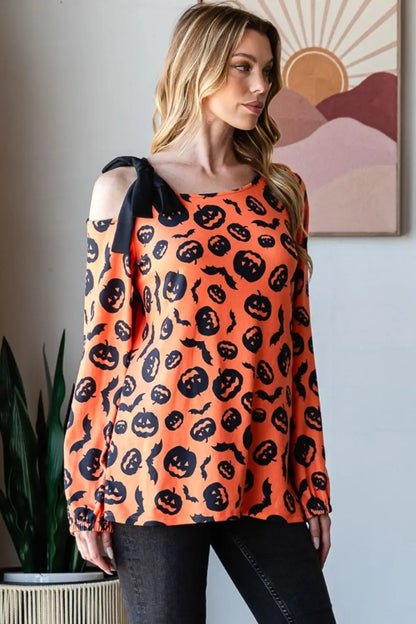 Woman wearing an orange Heimish pumpkin print one-shoulder t-shirt with black bow detail and Halloween-themed designs