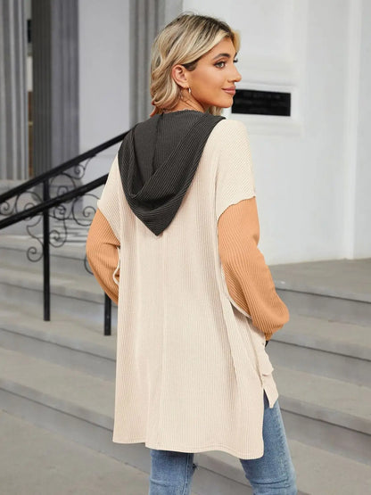 Woman wearing a Double Take Contrast Hooded Long Sleeve Top with beige body, tan sleeves, and black hood standing outdoors by stairs