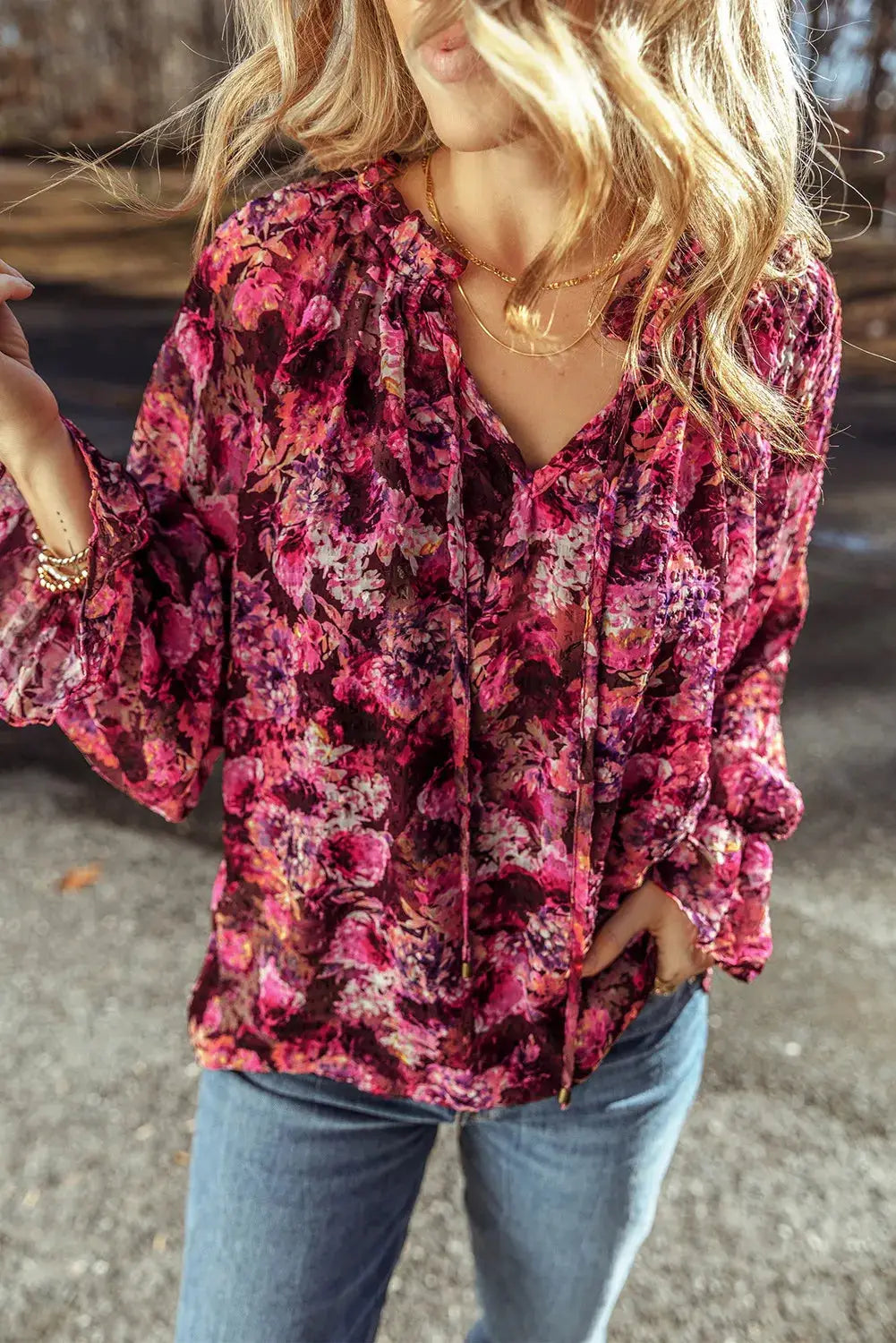 Woman wearing a vibrant printed tie neck blouse with flounce sleeves and ruffled sheer fabric in outdoor setting