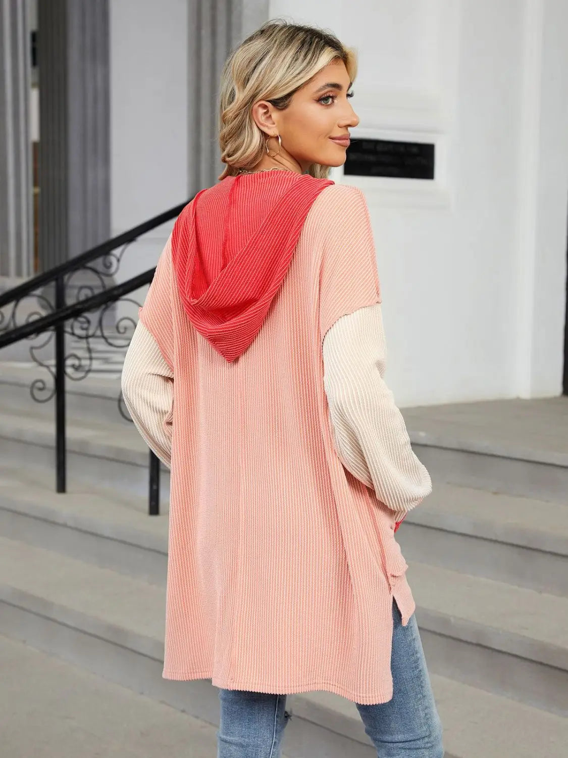 Woman wearing a pastel pink and cream contrast hooded long sleeve top with coral hood and pockets outdoors on steps