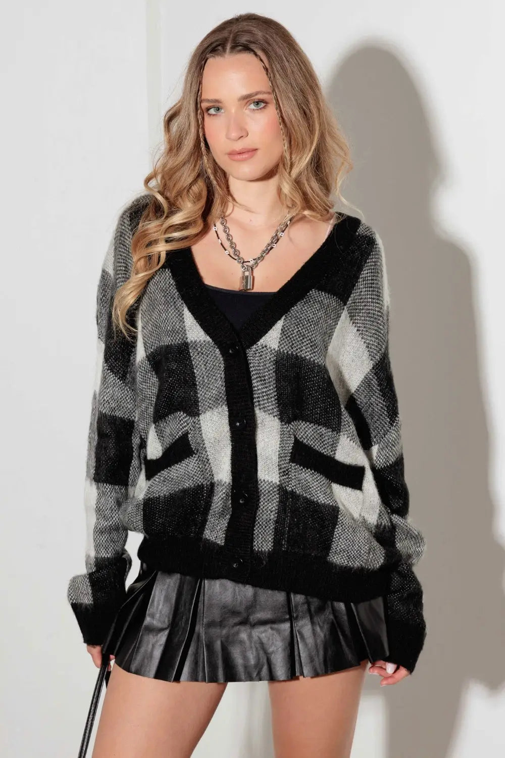 Woman wearing a black and white checkered V-neck cardigan with pockets and a black pleated mini skirt.