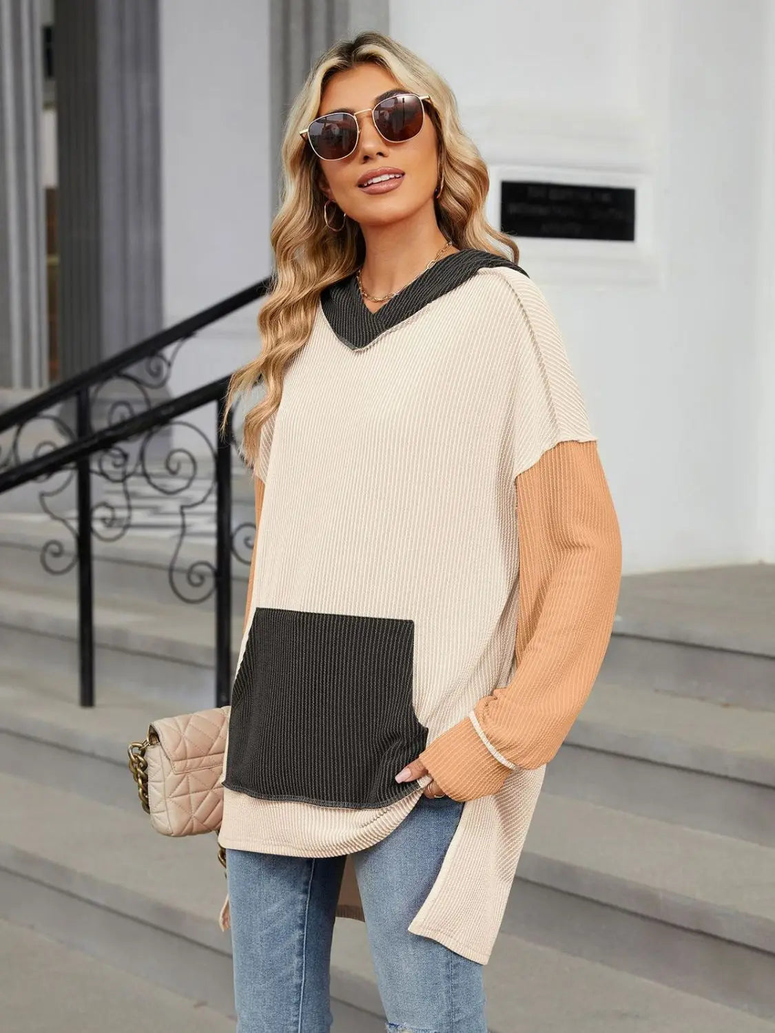 Woman wearing a Double Take Contrast Hooded Long Sleeve Top with beige, black, and tan color blocks and front pocket outdoors.