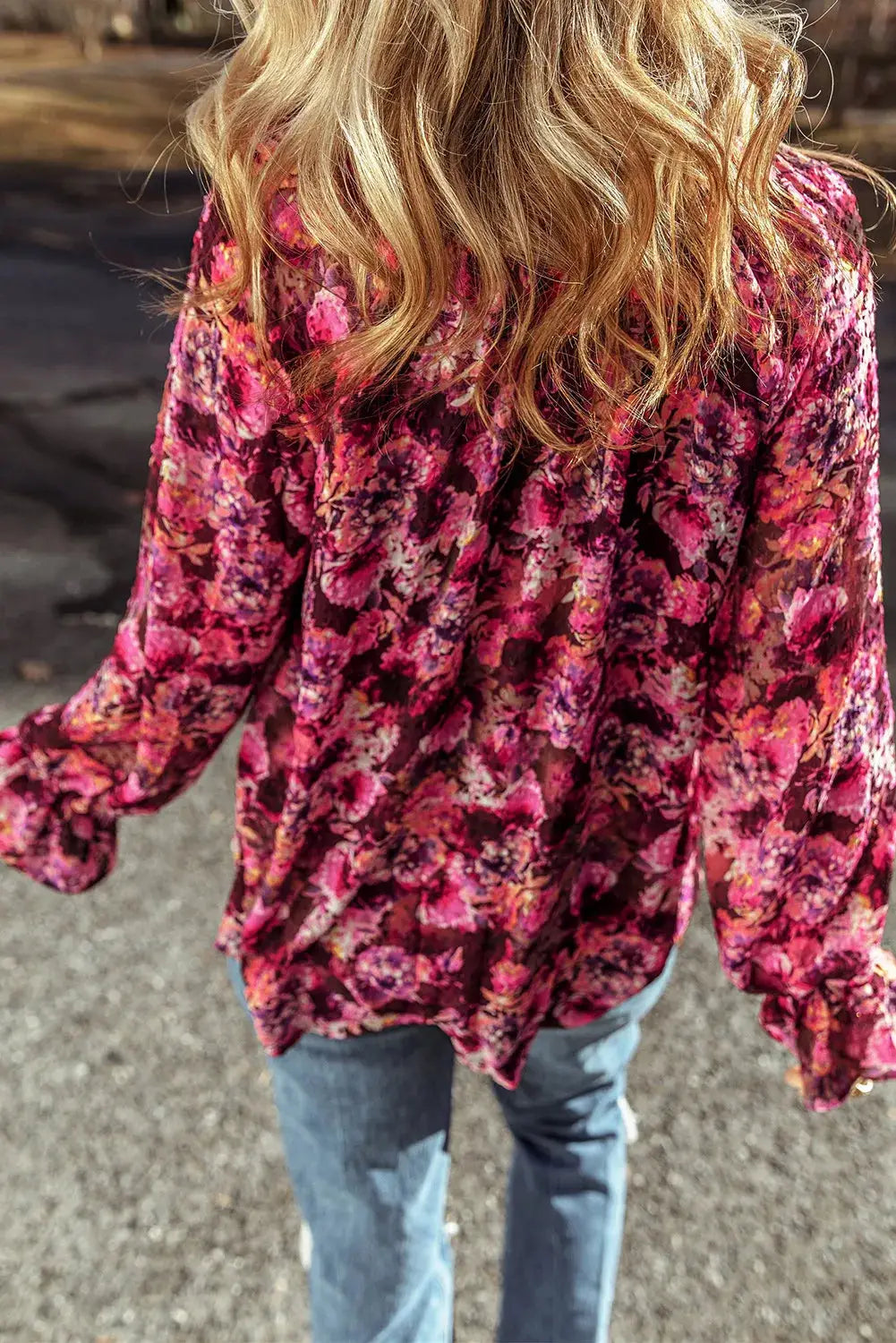 Woman wearing a vibrant pink printed tie neck blouse with flounce sleeves and ruffled floral pattern viewed from behind.