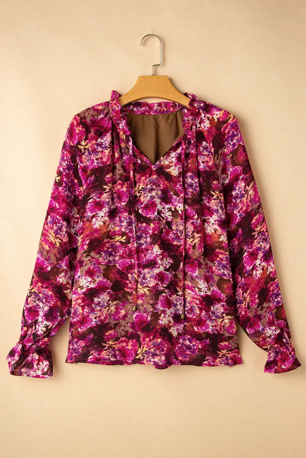 Printed tie neck blouse with flounce sleeves in vibrant pink and purple floral pattern hanging on wooden hanger