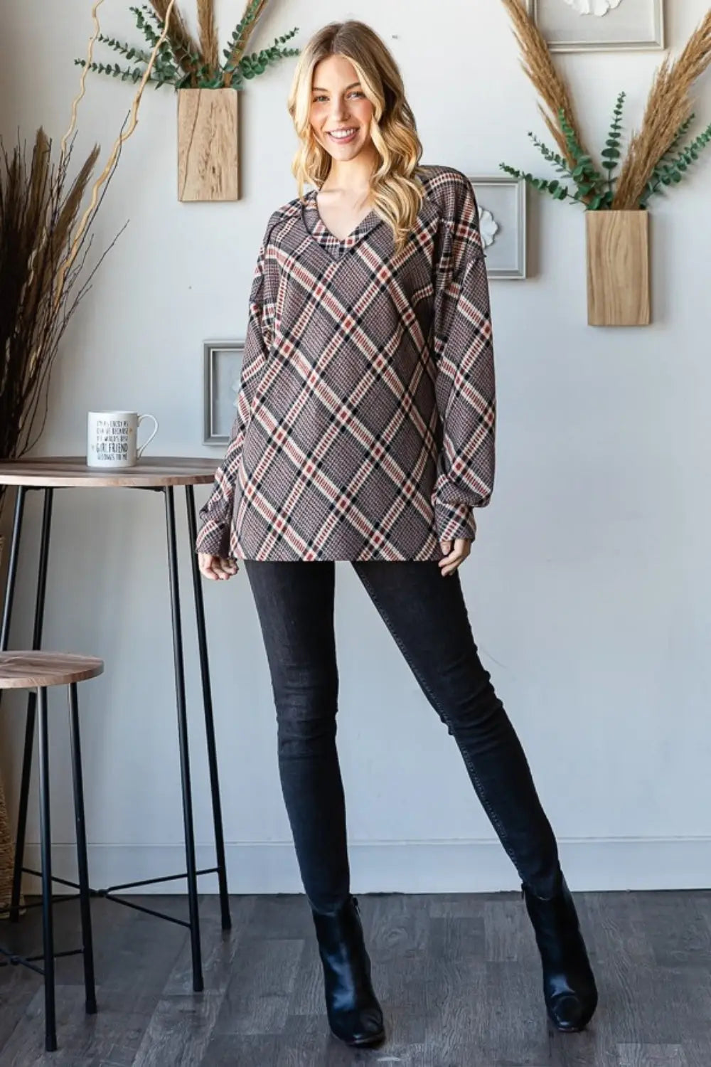 Woman wearing Heimish plaid exposed seam V-neck t-shirt paired with black skinny jeans and black ankle boots standing indoors