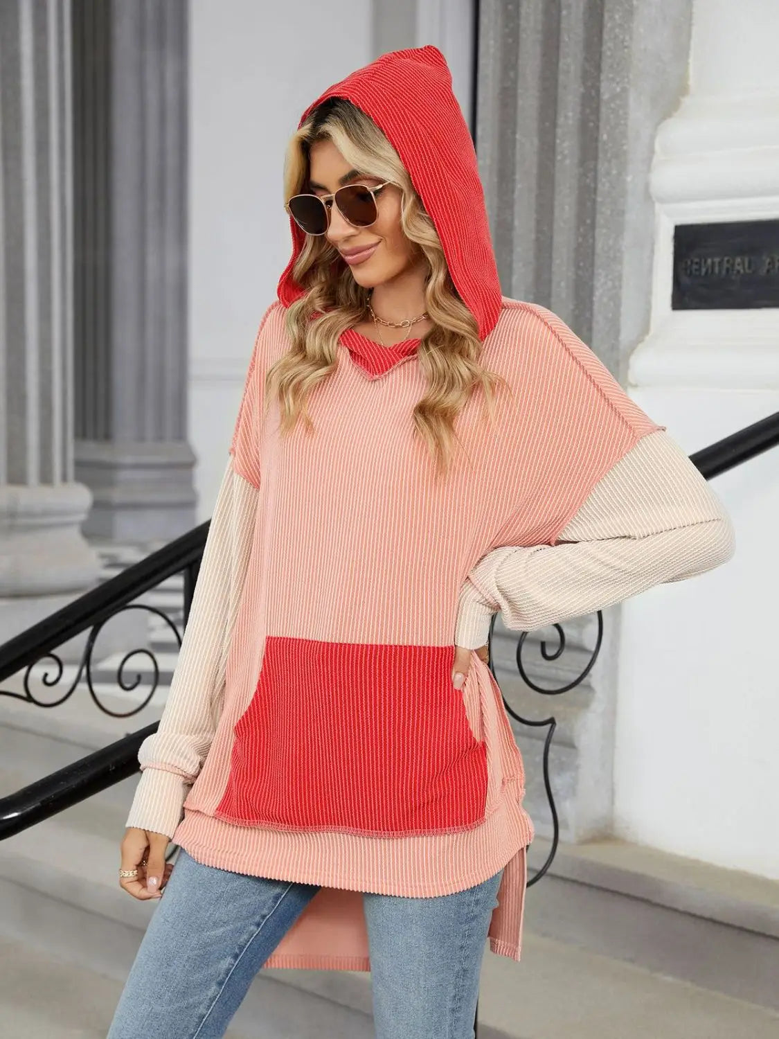 Woman wearing a color block ribbed hooded long sleeve top with front pocket and sunglasses outdoors