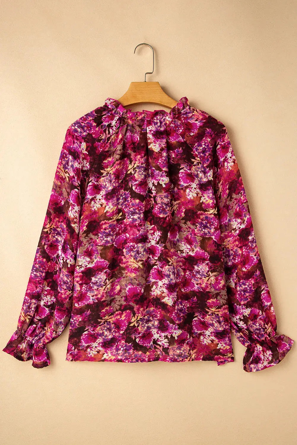 Printed tie neck blouse with flounce sleeves in vibrant purple and pink floral pattern hanging on wooden hanger.