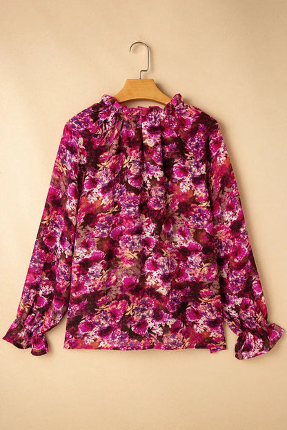 Printed tie neck blouse with flounce sleeves in vibrant purple and pink floral pattern hanging on wooden hanger.