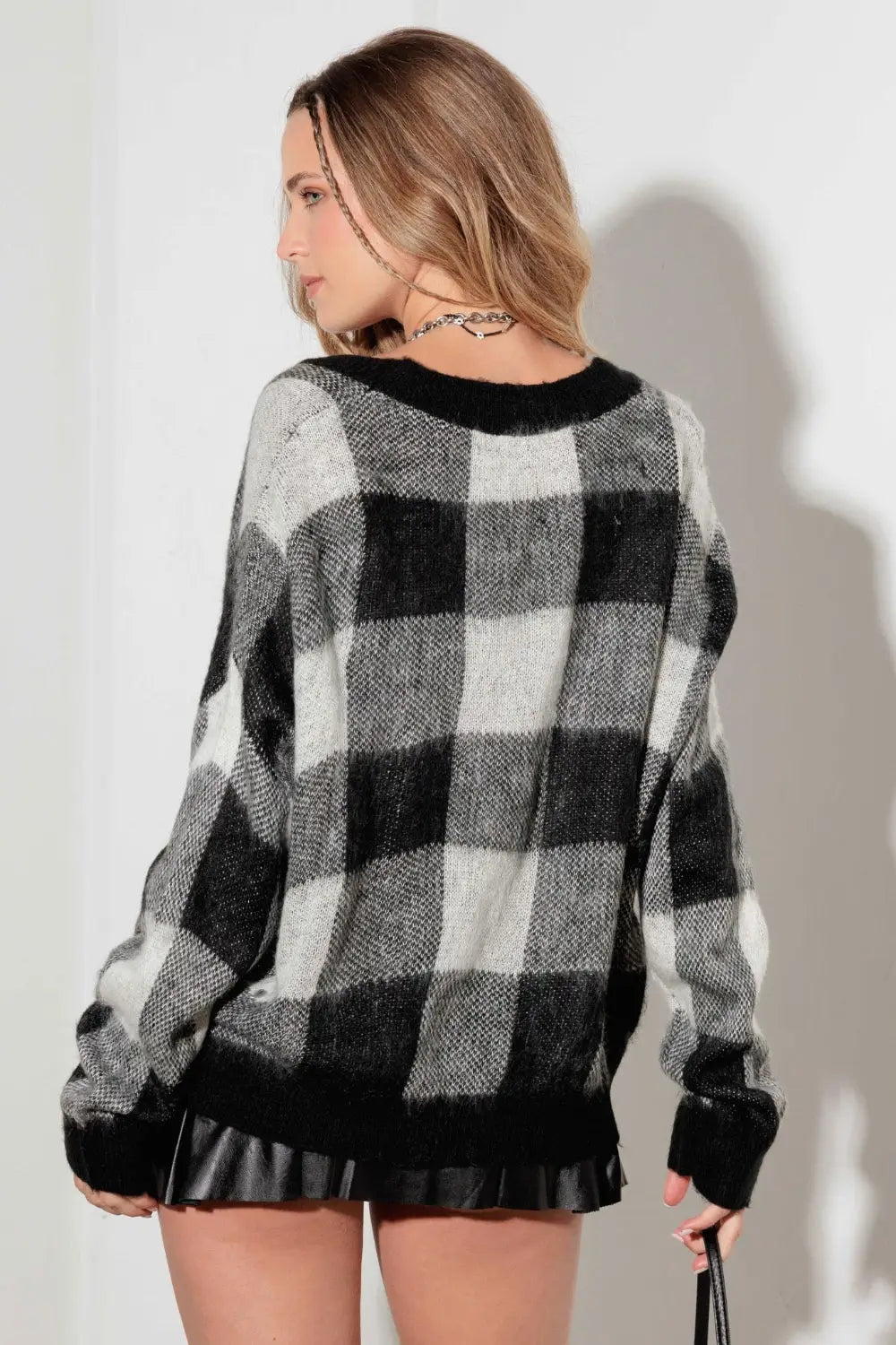 Woman wearing a black and white checkered V-neck cardigan with pockets and black trim at hem and cuffs