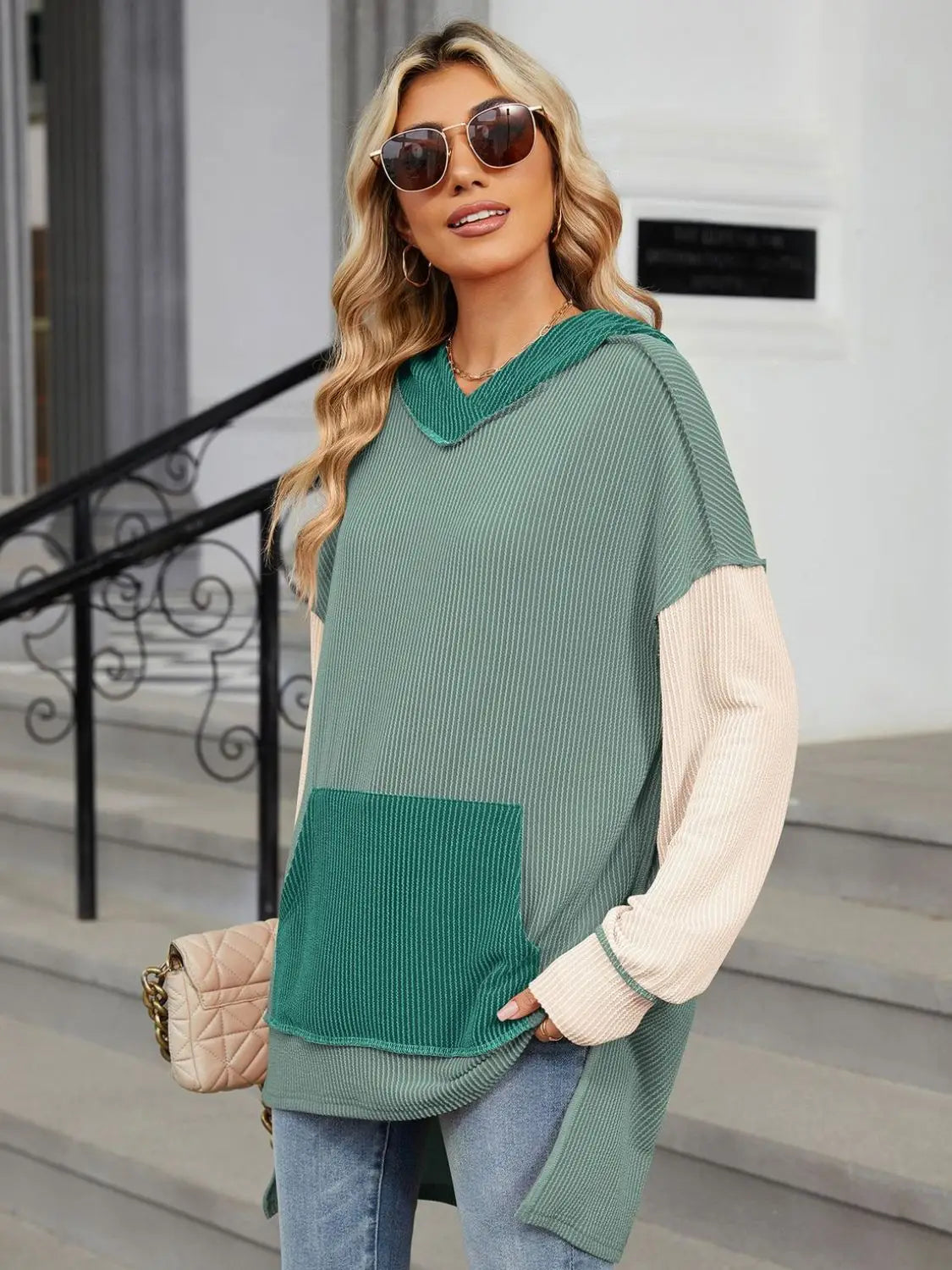 Woman wearing a Double Take Contrast Hooded Long Sleeve Top with green and beige ribbed fabric and front pocket outdoors