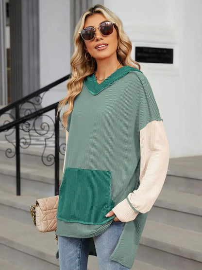 Woman wearing a Double Take Contrast Hooded Long Sleeve Top with green and beige ribbed fabric and front pocket outdoors