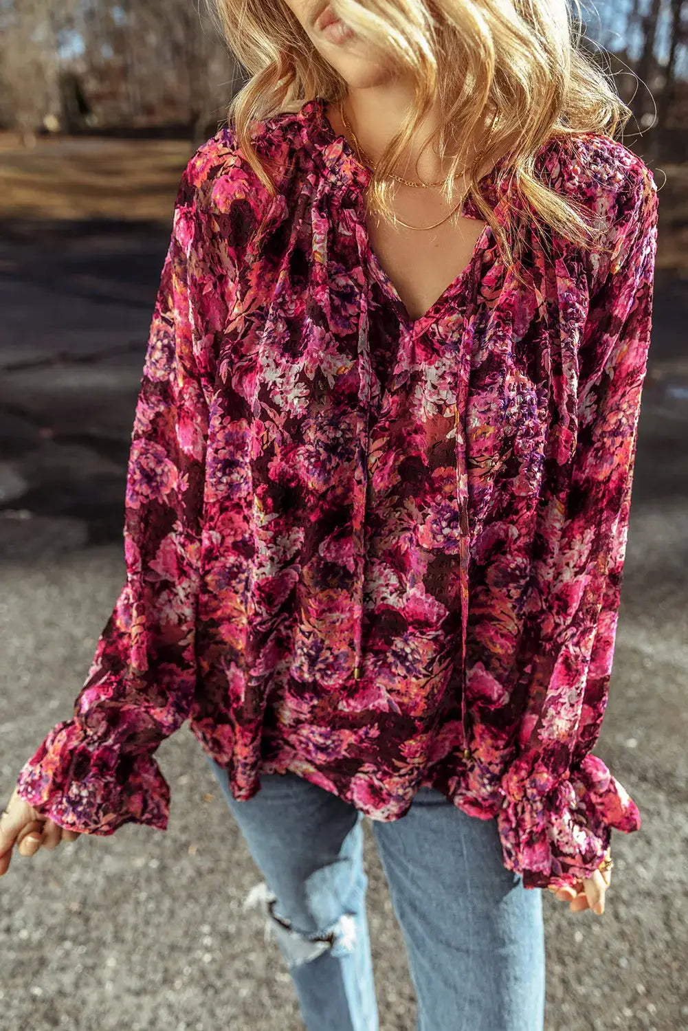 Woman wearing a vibrant printed tie neck blouse with flounce sleeves paired with ripped light blue jeans outdoors